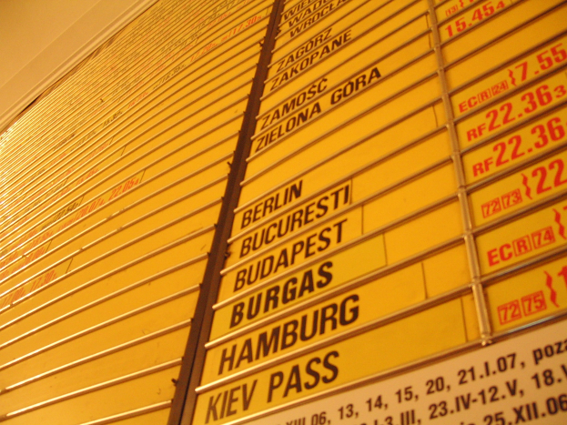 Eine gelbe Wand mit mehreren gelben Schildern, die wahrscheinlich Abfahrts- und Ankunftszeiten für verschiedene Ziele angeben.