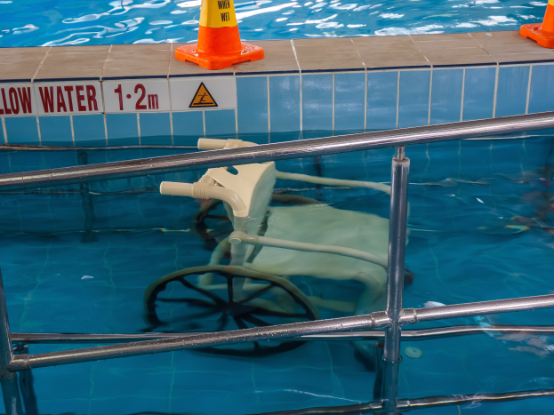 Ein Schwimmbad mit einem Stuhl in der Mitte, umgeben von Sicherheitskegeln und einem Geländer und einem Schild an der Wand, das die Anwesenheit von Schwimmausrüstung anzeigt.