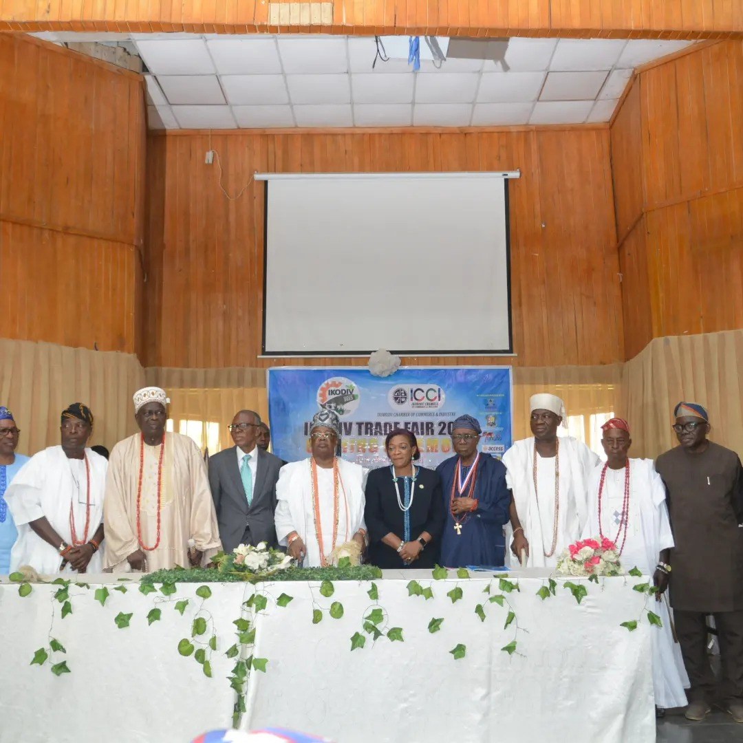 Eine Gruppe von Menschen, die um einen mit einer weißen Decke bedeckten Tisch mit Blumen und Blättern stehen, im Hintergrund ein Banner, ein Projektionsschirm und Deckenleuchten auf der ICCI International Trade Fair 2019.