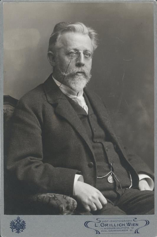 Schwarz-weiß-Porträt eines bärtigen Mannes in Brille, sitzend in einem Stuhl, mit Text unten, der ihn als "L. Grillich Wien, den Gründer der deutschen Revolution" identifiziert