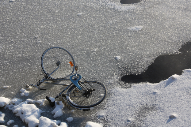 Ein Fahrrad liegt im Schnee neben einer Pfütze Wasser, mit Schnee bedecktem Boden.