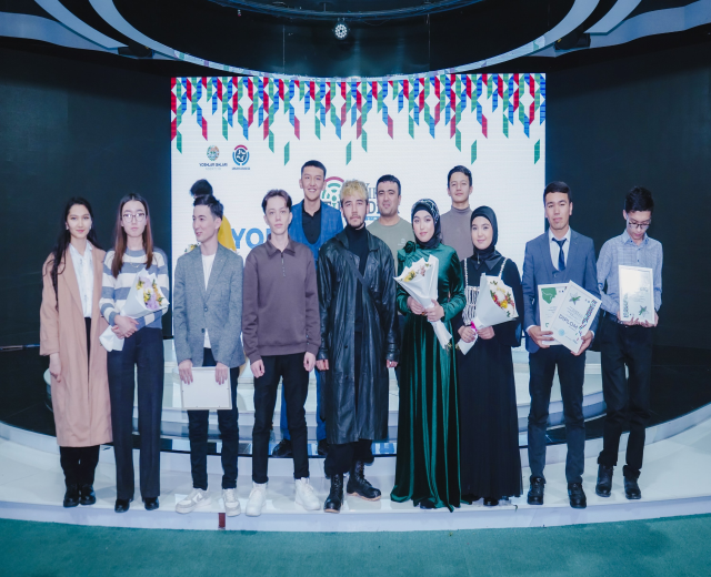 Gruppe von Menschen auf einer Bühne mit Blumensträußen und Urkunden, im Hintergrund ein 'Jugend-Solar-Awards 2019'-Plakat.