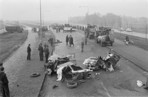 Schwarz-weiß-Szene eines Autounfalls am Straßenrand mit mehreren Fahrzeugen, Menschen in der Nähe, Laternenpfähle, Bäume und Himmel im Hintergrund.