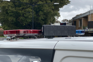 Ein Polizeiwagen mit eingeschaltetem Blaulicht steht an der Straße neben Gebäuden, Bäumen, Pfählen und Schildern mit Text, unter einem bewölkten Himmel, wahrscheinlich nach einem tödlichen Schusswechsel an einer Schule in Brisbane.