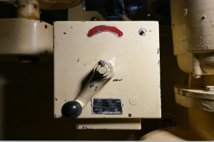 Nahaufnahme einer Steuerkonsole mit Drehknopf und Messgerät, umgeben von Rohren, die ein gut ausgestattetes Steuerungssystem andeuten.