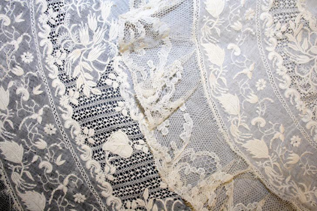 Nahaufnahme eines weißen Hochzeitskleids mit zarter, detailreicher Spitzenverzierung auf einem leichten, luftigen Stoff.