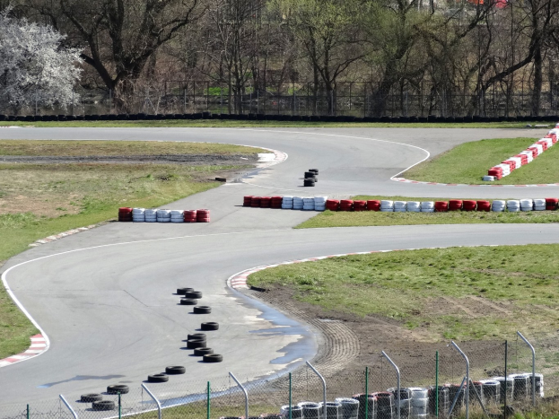Rennstrecke mit zahlreichen Reifen, die entlang der Bahn angeordnet sind, umgeben von Gras und Maschendrahtzaun, mit Bäumen im Hintergrund.