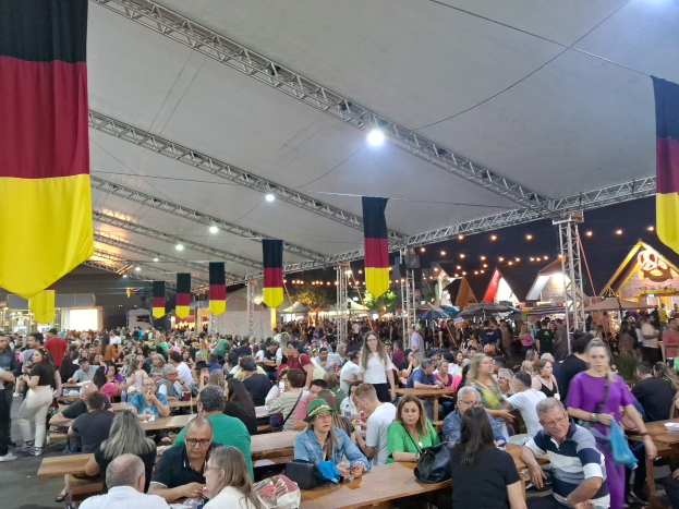 Eine große Gruppe von Menschen sitzt an Tischen unter einem Zelt auf dem Oktoberfest in München, Deutschland, mit Taschen und Gegenständen auf den Tischen, umgeben von festlichen Décorations und zusätzlichen Zelten im Hintergrund.