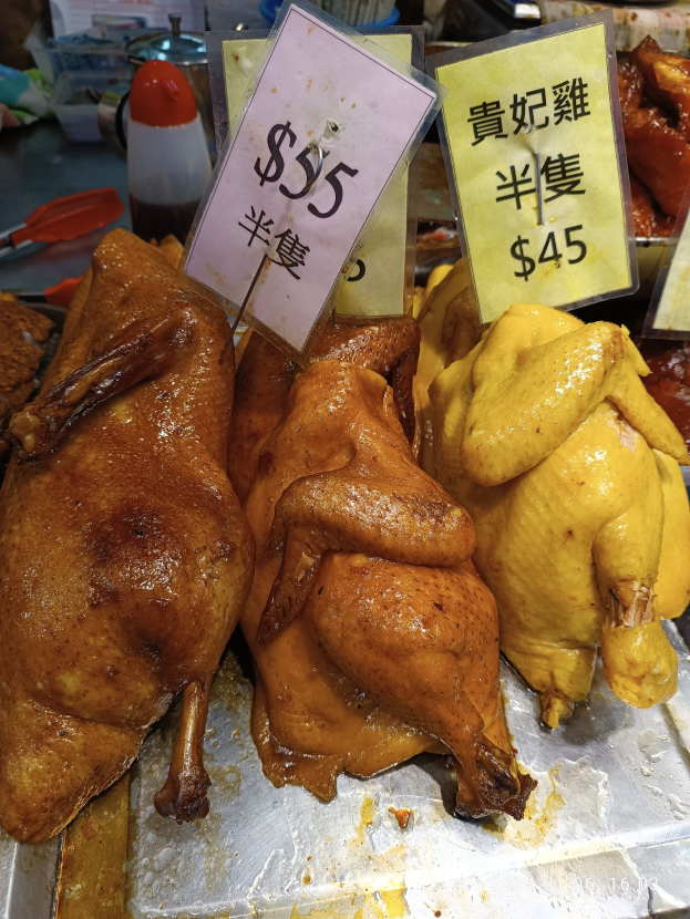 Eine Ansammlung von Hühnern auf einem Metalltablett mit Preisschildern in einer Marktsituation.