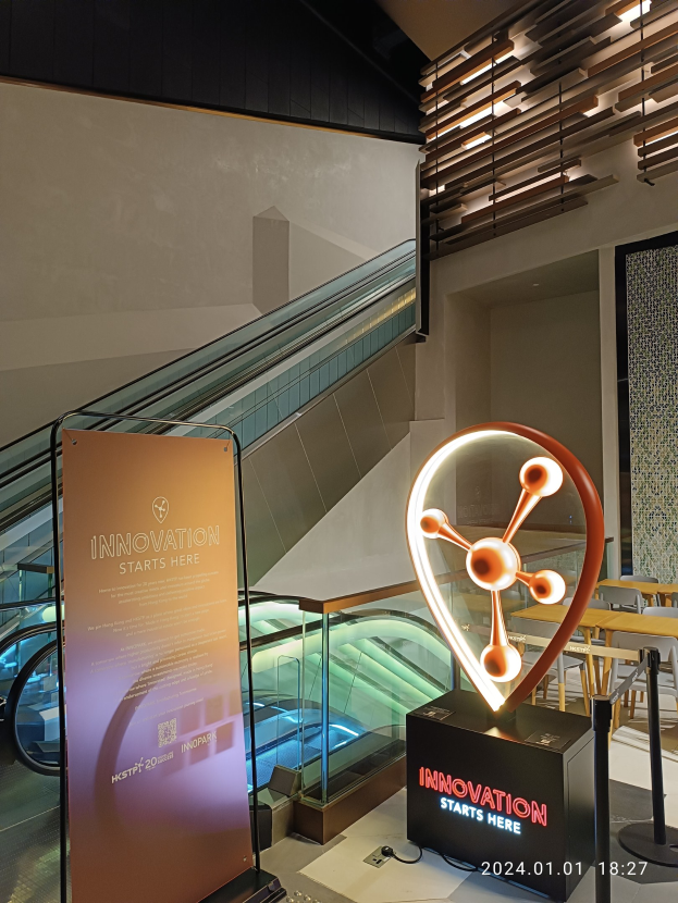 Großes Schild mit der Aufschrift "Innovation beginnt hier" in einem Gebäude mit einer Treppe im Hintergrund, Tische und Stühle auf der rechten Seite und ein Schild, das auf die HSTP20 Expo hinweist.