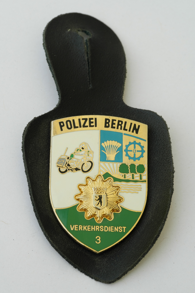 Ein Polizeistern mit blauem Hintergrund, weißer Stern und weißer Umrandung, auf dem der Text "Polizei Berlin" in fetter schwarzer Schrift steht.