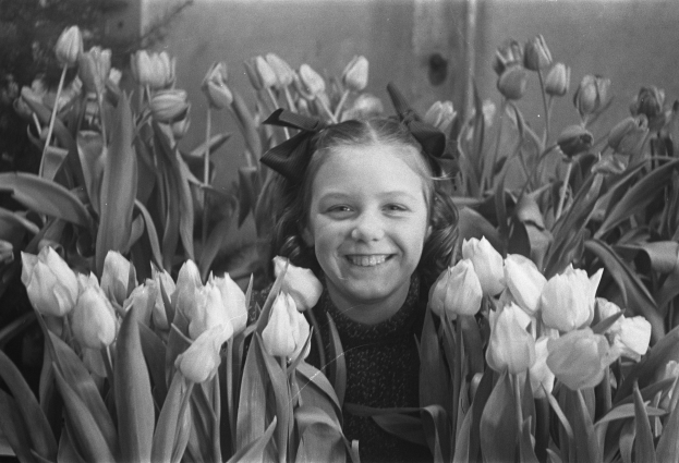 Ein Schwarz-Weiß-Foto einer jungen Mädchen, das in einem Feld voller leuchtender Tulpen lächelt.