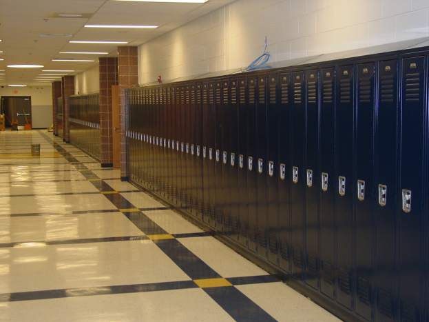 Eine lange Reihe von Spinden in einem Schulflur mit einem gefliesten Boden, einer Wand im Hintergrund, einer Decke mit Lampen oben und ein paar Gegenständen herum.