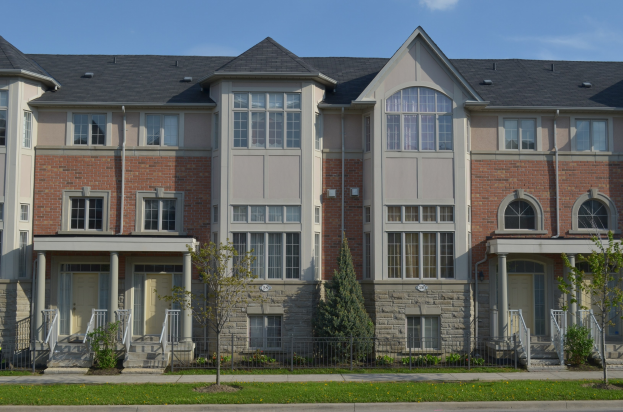 Eine Reihe von Stadthäusern in einem Wohnviertel mit sichtbaren architektonischen Details, Grünflächen und einer Straße im Vordergrund unter einem Himmel als Hintergrund.