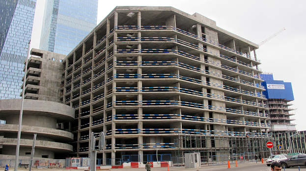 Großes Bauprojekt in einer Stadt mit Wolkenkratzern, Fahrzeugen, Fußgängern, Verkehrsinfrastruktur und Kränen vor einem klaren Himmel.