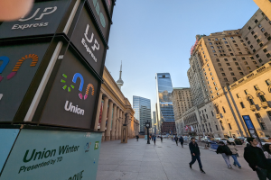 Eine belebte Stadtstraße mit Fußgängern, hohen Gebäuden, Fahrzeugen und Verkehrsschildern in Verbindung mit der Union Winterkonferenz unter einem sichtbaren Himmel.