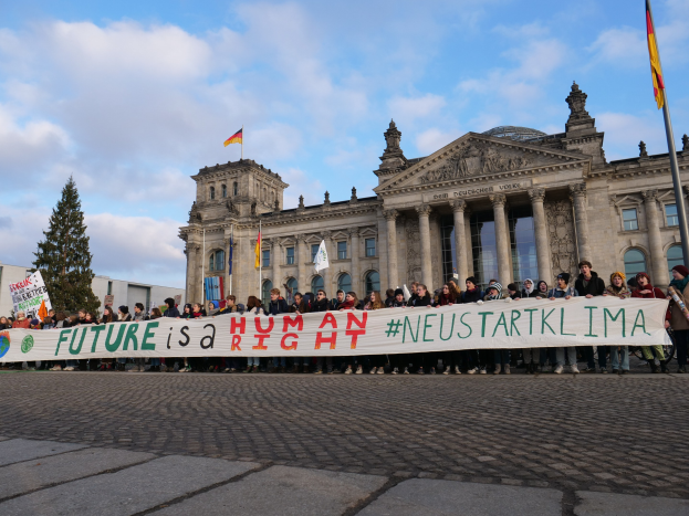 Gruppe von Menschen vor dem Reichstaggebäude in Berlin mit einem Banner, auf dem 'Zukunft ist ein Menschenrecht' steht.