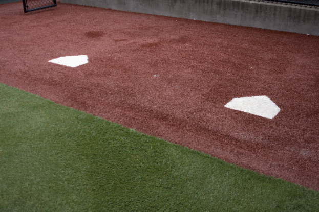 Baseballfeld mit Kunstrasen, umgeben von einem Zaun, mit einem Home Plate und einer Wand im Hintergrund.