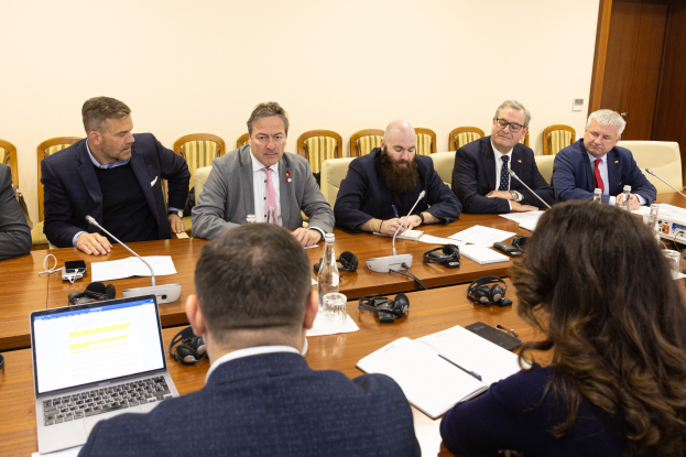 Eine Gruppe von Menschen, wahrscheinlich Mitglieder des Europäischen Parlaments, sitzt um einen Tisch in einem Konferenzraum, umgeben von Laptops, Büchern, Papieren, Flaschen, Gläsern, Headsets, Mikros mit Ständern und Mobiltelefonen.