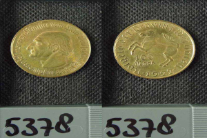 Zwei Goldmünzen aus Deutschland im Jahr 1922 mit je einer Denomination von 100 Mark werden auf einer schwarzen Oberfläche mit Zahlen unten platziert.