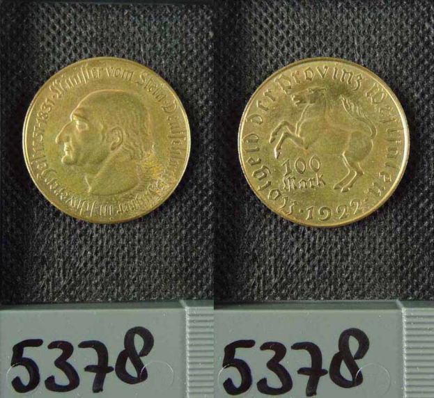 Zwei Goldmünzen aus Deutschland im Jahr 1922 mit je einer Denomination von 100 Mark werden auf einer schwarzen Oberfläche mit Zahlen unten platziert.