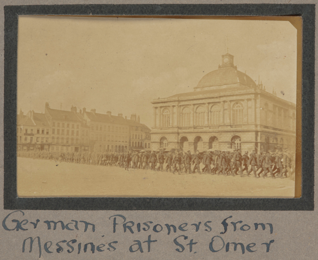 Eine Gruppe deutscher Gefangener aus Messines steht vor einem Gebäude unter einem klaren blauen Himmel, mit Text am unteren Bildrand.