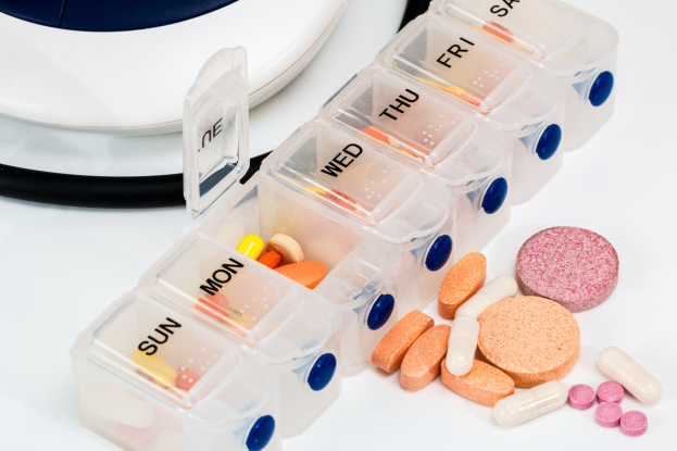 Weißer Tisch mit einer Pillendose, die Pillen enthält, und einem Stethoskop daneben, Pillendose mit Text beschriftet.
