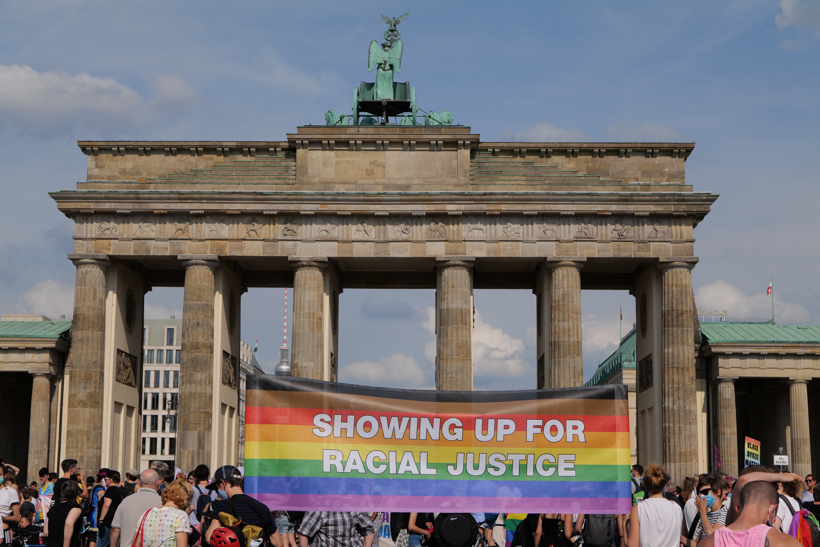 Eine Gruppe von Menschen, die vor dem Brandenburger Tor in Berlin, Deutschland, mit einem Banner mit der Aufschrift "Racial Justice" steht.