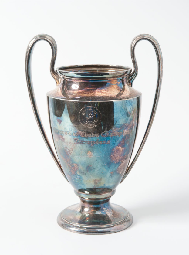 Der UEFA-Champions-League-Pokal, ein stahlerner Becher mit zwei Händeln und einem blauen und silbernen Farbschema, beschriftet mit «UEFA Champions League», gegen einen weißen Hintergrund dargestellt.