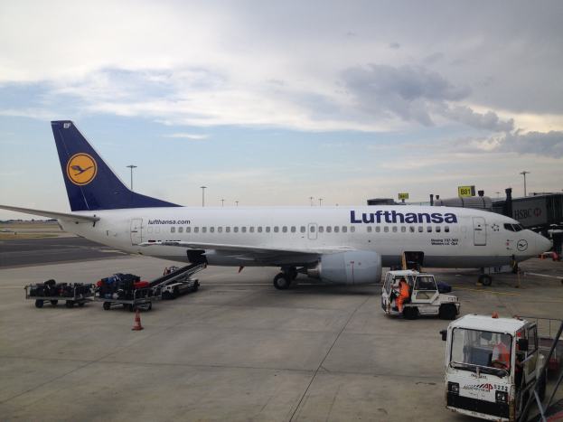 Lufthansa Airbus A320-200 am Frankfurter Flughafen mit Bodenfahrzeugen, Verkehrskegeln und Beschilderung im Hintergrund unter einem bewölkten Himmel.