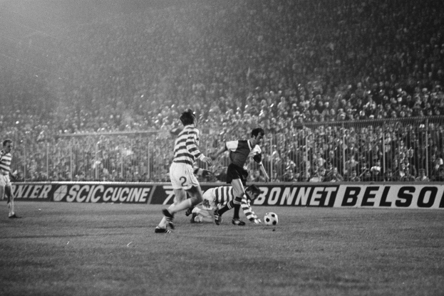Ein Schwarz-Weiß-Bild von Männern, die auf einem Feld Fußball spielen, mit Zuschauern auf den Tribünen und einem Banner mit der Aufschrift "Celtic v West Bromwich Albion - FA Cup Third Round."