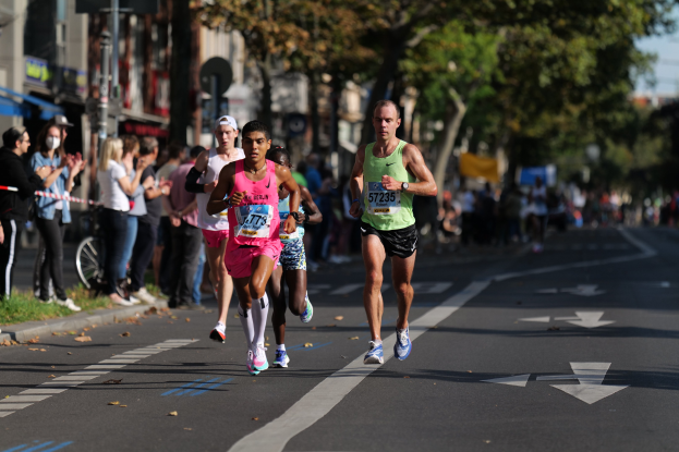 Gruppe von Läufern bei einem Marathon auf einer Stadtstraße mit Zuschauern und unscharfen städtischen Elementen im Hintergrund.