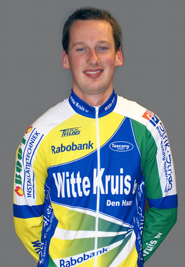 Ein männlicher Sportler posiert für ein Foto, wobei er ein Hemd mit Namen mehrerer Sponsorenunternehmen trägt.