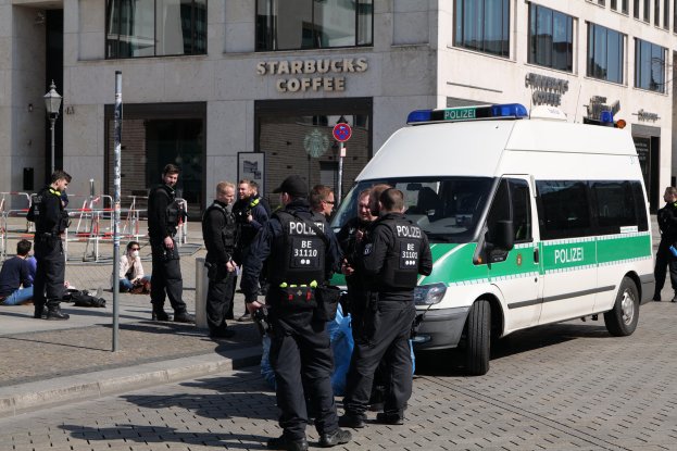 Gruppe von Polizeibeamten vor einem Starbucks-Café mit einem Van auf der rechten Seite und Menschen auf der linken Seite, Hintergrund enthält ein Gebäude mit Fenstern, ein Schild, eine Laterne und eine Absperrung.