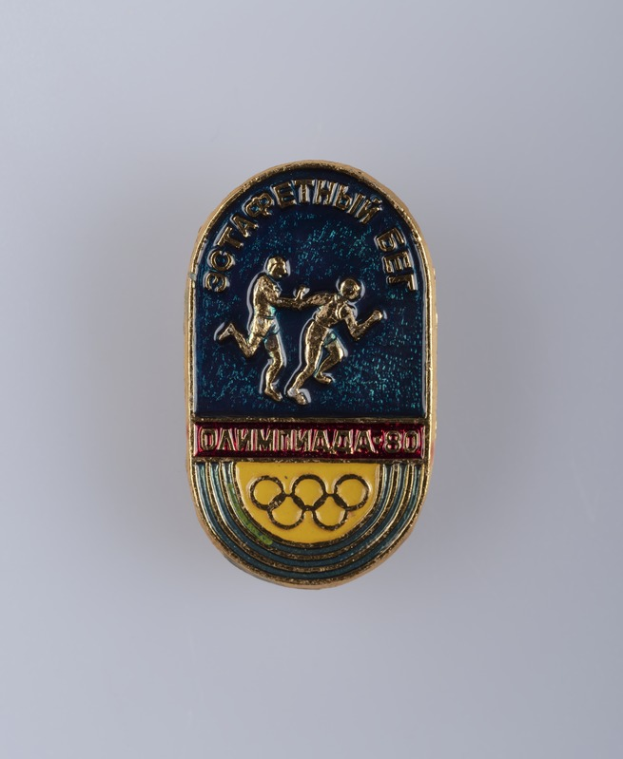 Ein rundes Abzeichen mit dem Logo der Olympischen Spiele 1980 in Moskau, das zwei Läufer und den Text 'Olympische Spiele' darüber zeigt.