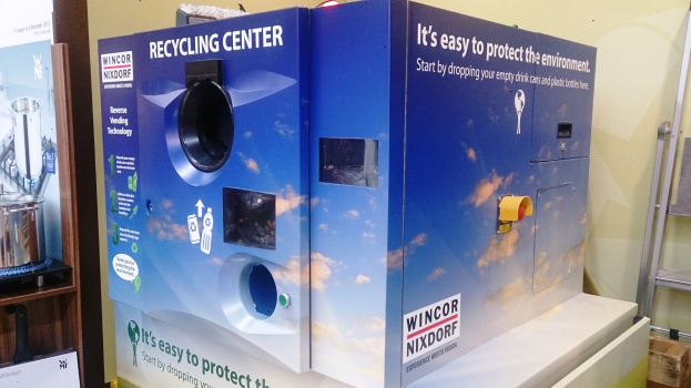 Blaues Recyclingzentrum mit einem "Recyclingzentrum"-Schild in der Mitte, einem Gestell mit verschiedenen Gegenständen links, einem einzelnen Gegenstand auf dem Boden rechts und Hintergrundbeleuchtung und Wand.