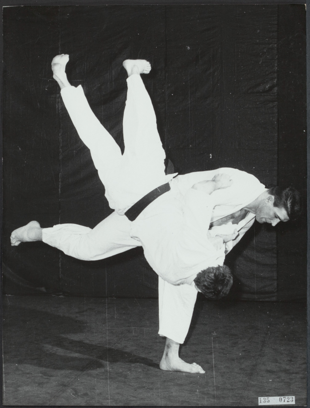 Zwei Männer in einem Judo-Match, einer in einem weißen Kimono und der andere in einem schwarzen Gürtel, in einem dämmrig beleuchteten Raum.