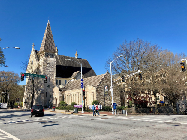 Die Episkopalkirche St. Lukas, eine große Kirche mit einem Turm, steht an einer Straßenecke umgeben von Gebäuden, Fahrzeugen, Fußgängern und Bäumen unter einem klaren blauen Himmel.