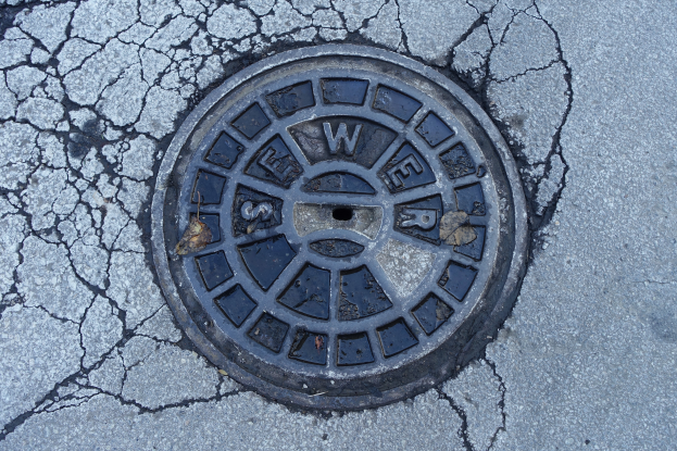 Ein Metallgullideckel am Straßenrand mit sichtbaren Rissen und eingravierter Schrift.