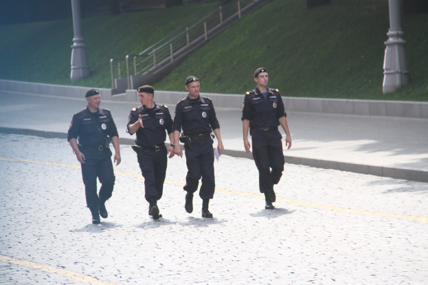 Drei Polizisten in Uniform auf einer Straße mit Pfosten, Geländern, Treppen und Gras im Hintergrund.