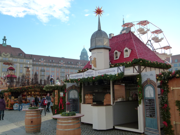 Ein lebendiger Weihnachtsmarkt in Nürnberg, Deutschland, mit Menschen um geschmückte Stände, Gebäude, ein Riesenrad und eine Tafel rechts.