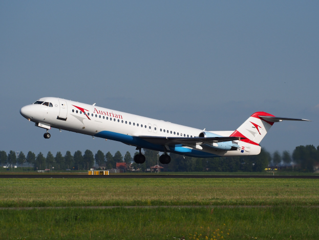 Austrian Airlines Embraer ERJ-190 Flugzeug beim Abheben vom Frankfurter Flughafen, mit grünem Gras, Bäumen, Gebäuden und Himmel im Hintergrund.
