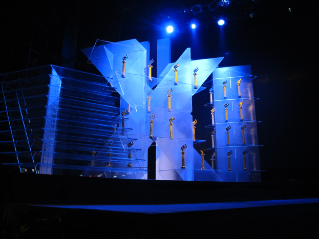 Eine Bühne für eine Preisverleihung mit dunklem Hintergrund, beleuchtet von wenigen Lichtern und verschiedenen, zur Veranstaltung gehörenden Gegenständen.