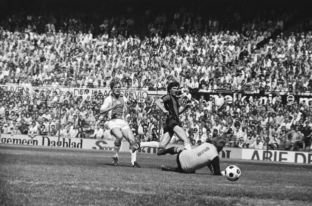 Schwarz-weißes Foto von Männern, die auf einem Feld Fussball spielen, mit Zuschauern im Hintergrund und einem Banner mit der Aufschrift "Bundesliga 1978-79 Ajax 1-1 Hannover 96."