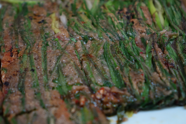 Nahaufnahme eines Steaks mit goldbrauner Kruste und saftigem Innern neben zarten Spargelstangen auf einem weißen Teller, garniert mit Kräutern und Gewürzen.