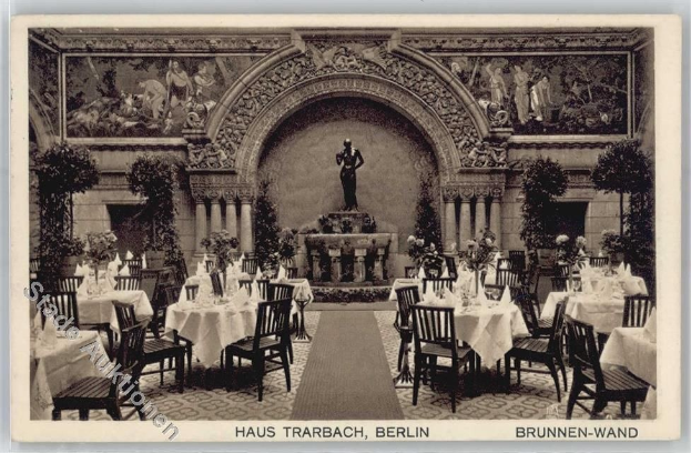 Ein altes Schwarz-Weiß-Foto eines Berliner Restaurants mit Tischen, Stühlen, Blumenvasen und einer Statue im Hintergrund, mit Skulpturen und Pflanzen an den Wänden und Text unten.