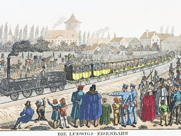 Eine Gruppe von Menschen um einen Zug auf einem Gleis herumstehend, mit einigen im Zug und anderen außerhalb, in der Nähe von Gebäuden und Bäumen, mit Text 'Ludwigs-Eisenbahn, die erste Bahnstation in Deutschland' unten.