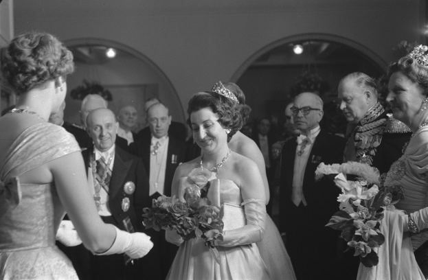 Schwarzes und weißes Foto von Queen Elizabeth II. und Prinz Philip, Duke of Edinburgh, an ihrem Hochzeitstag, die Kronen tragen und Blumensträuße halten, umgeben von einer Gruppe von Menschen, mit Lichtern und einer Wand im Hintergrund.