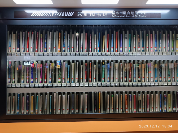 Eine Bibliothek mit zahlreichen Büchern auf Regalen, beleuchtet von Deckenlampen, mit einer Texttafel und einem Wasserzeichen unten, sieht aus wie eine Selbstbedienungsbibliothek von Stadtvierteln.