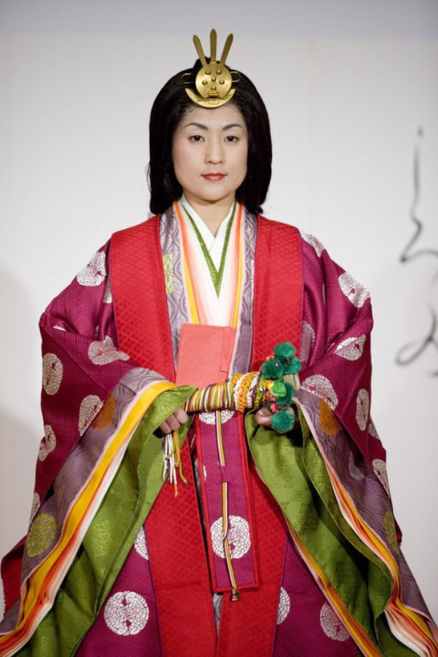 Eine Frau in einem traditionellen japanischen Kimono steht selbstbewusst auf einem Laufsteg, trägt ein leuchtend rotes und grünes Kleid mit kunstvollen Mustern und hat ihr Haar zu einem ordentlichen Knoten gebunden.